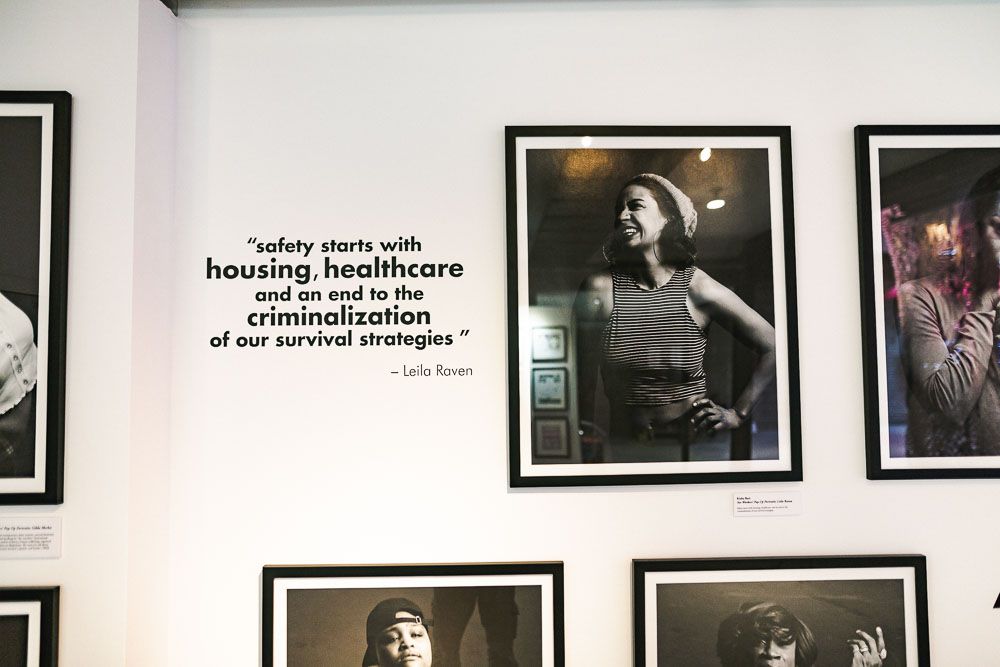 A wall of photographs at the exhibit and a quote from Leila Raven that says "safety starts with housing, healthcare and an end to the criminalization of our survival strategies."